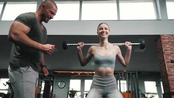 Attractive Girl in a Gray Sports Coat Does Exercises with Dumbbells at the Gym