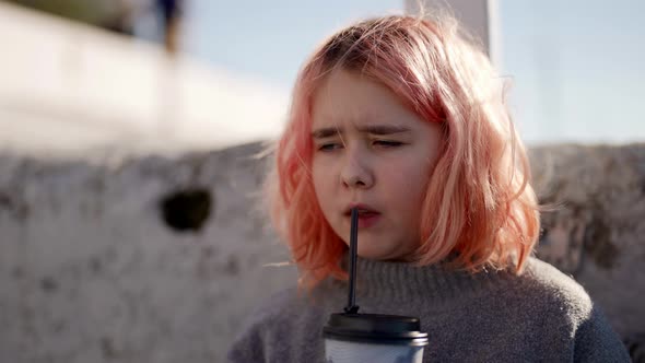 Sad Little Girl is Drinking Milkshake From Fast Food Restaurant on City Street Sipping By Straw