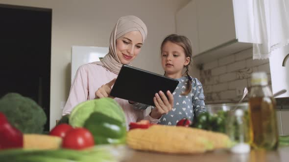 Excited Caucasian Little Girl with Muslim Mother Watching Salad Recipe on Tablet