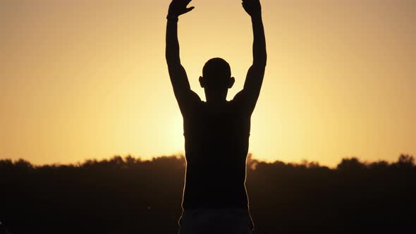 Silhouette of Young Man Against Sunset Raising Hands Sides and Up. Slow Motion