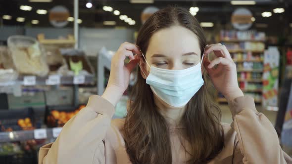 A Beautiful Girl Puts on a Medical Protective Mask in the Supermarket