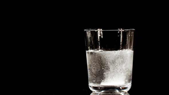 Pill Aspirin Falling Down in Glass with Water on Black Background