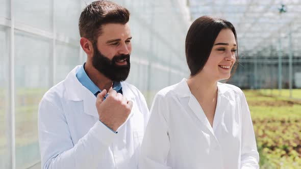 Two Researchers in Laboratory Robes Walk Around the Greenhouse