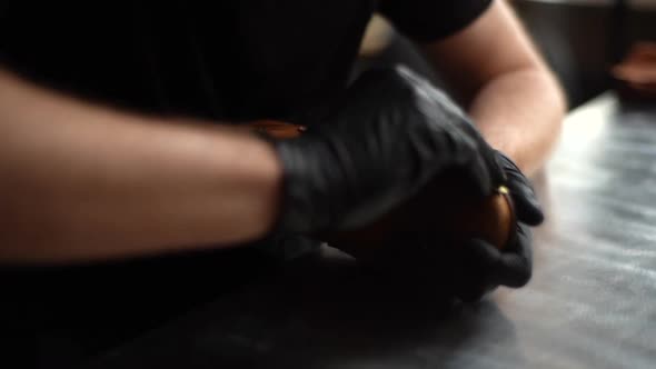 Close-up of shoemaker wearing black latex gloves cleaning old light brown leather shoes with rag.