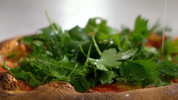 baker decorates fresh hot pizza with cheese from the oven with aromatic herbs