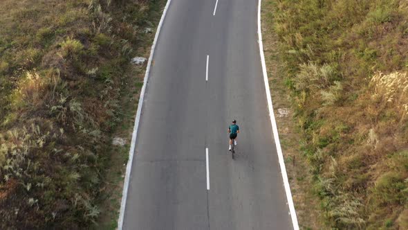 Aerial drone view of man cycling uphill along country road. 