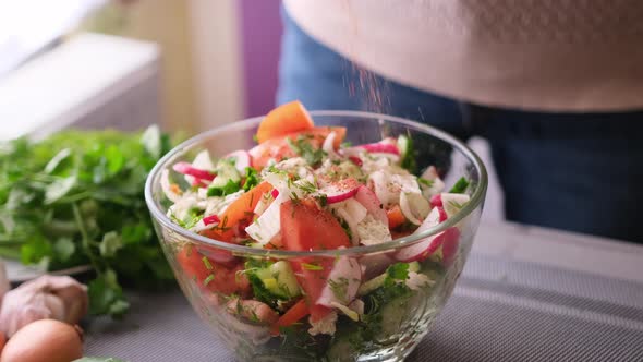 Woman Adding Salt and Spices Into Mixed Salad of Vegetables  Tomatoes Cucumbers Onion Parsley