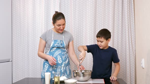 Boy Beats Eggs with a Whisk Under the Supervision of a Woman in the Kitchen