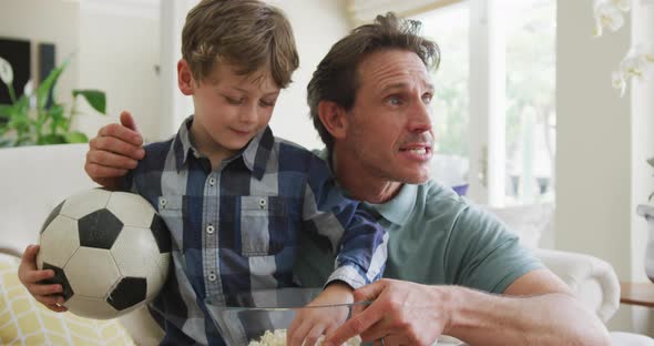 Happy caucasian father and son watching tv and supporting in living room