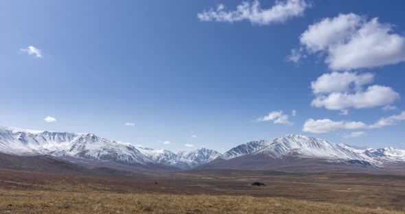 Timelapse of Sun Movement on Crystal Clear Sky with Clouds Over Snow Mountain Top. Yellow Grass at