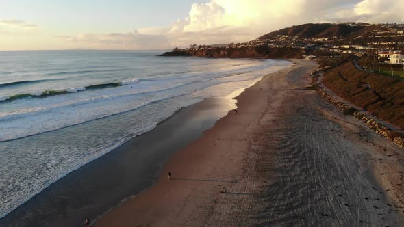 A drone flies down the coast revealing a stunning sunset at the beach.