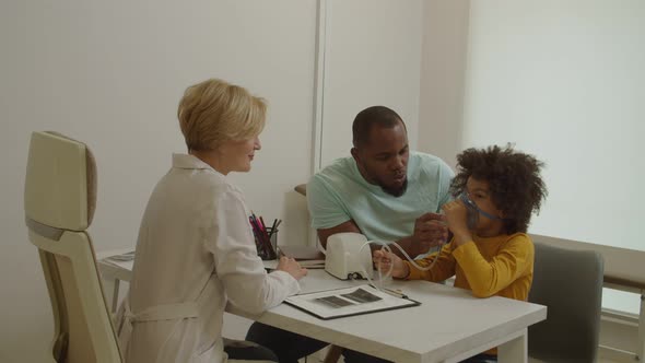 Cute Ill Preschool African American Boy Making Inhalation with Nebulizer at Medical Clinic