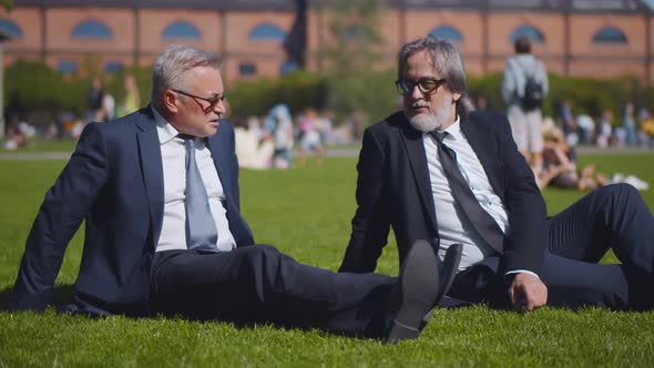 Successful Mature Entrepreneurs Relaxing on Green Lawn in Park and Chatting