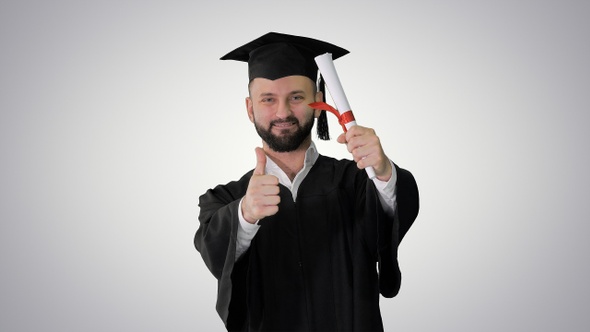 Young male smiling graduate showing thumb up on gradient