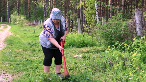 An Elderly Woman Mows Low Green Grass with an Electric Trimmer