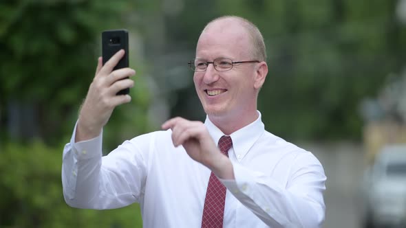 Happy Mature Bald Businessman Smiling and Taking Selfie Outdoors