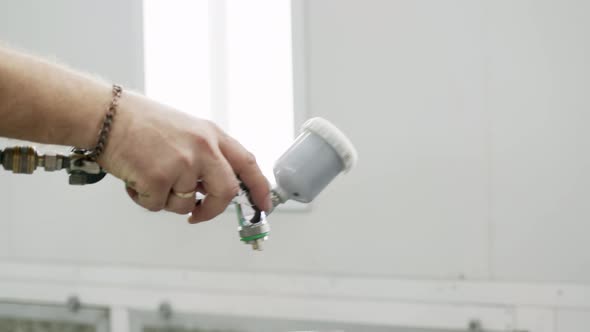 Close View of Spray Gun in Hands of Person Painter Painting Car or Other Thing in Spray Booth