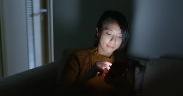 Woman use of mobile phone and sit on sofa at night