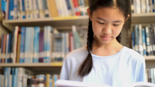 Asian teenager student reading a book in school library.