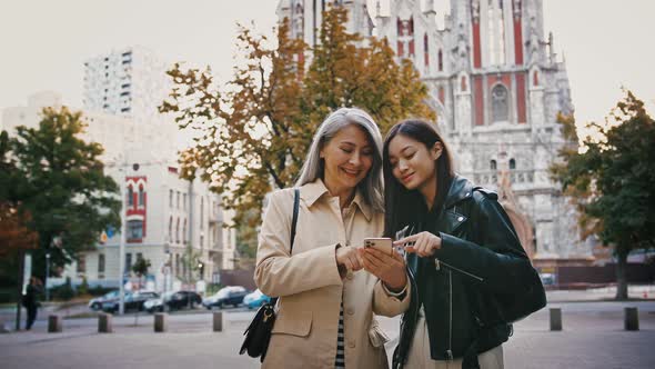 Asian Mature Mum and Adult Daughter are Using Smartphone While Standing in the City Square Smiling