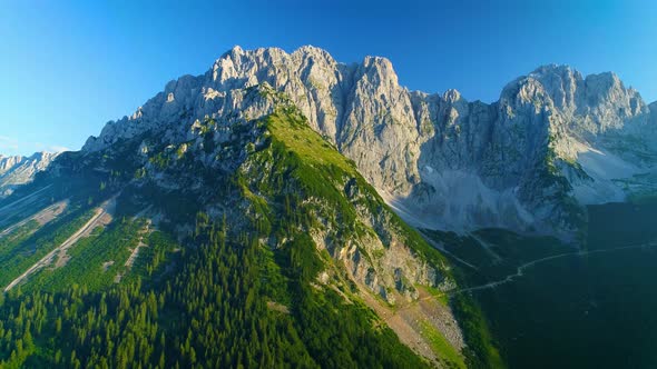 Stunning aerial view across woodland covered slopes of sunlit Wilder Kaiser mountains peaks