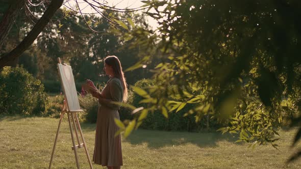 Creative Woman Artist Paints a Picture with a Brush While Standing Near the Easel in Nature