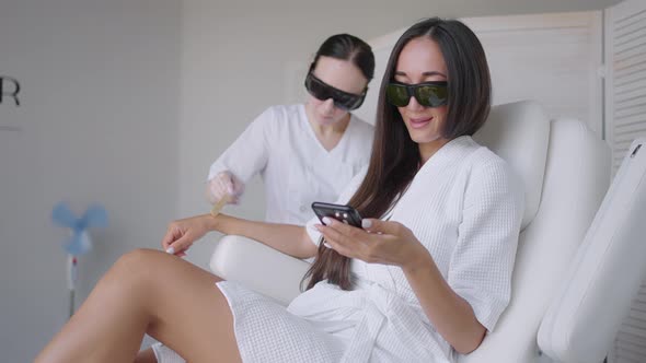 During a Laser Hair Removal Session a Woman in a Beauty Salon Writes a Message in Her Mobile Phone