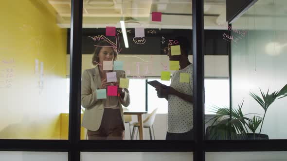 Two diverse female colleagues making notes and discussing at work