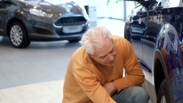 Senior Man Examines the Car Wheel at the Dealership