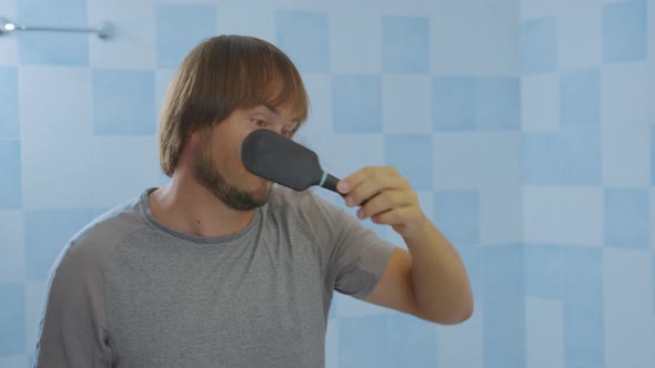 Man Looking in Bathroom Mirror Combing His Hair Styling or Checking for Hair Loss Problem. Male