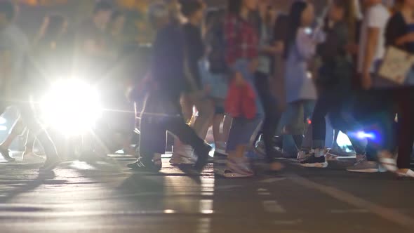 Crowd of People Crossing Street at a Crosswalk in the Evening. Cars with Lights on Standing