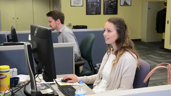 Two young professionals talking and working on computers in cubicles