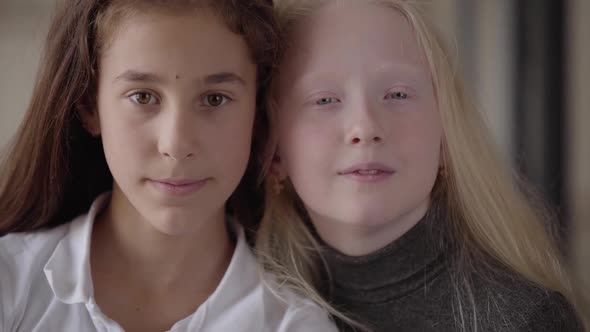 Close-up Portrait of Brunette Girl with Brown Eyes and Blonde Girl with Grey Eyes Looking at the