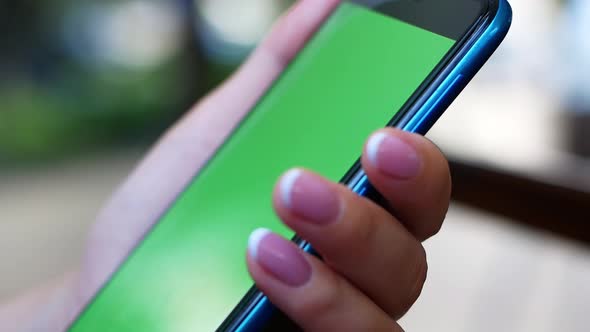 A woman is sitting in a cafe with a smartphone in her hands with a green screen mockup.