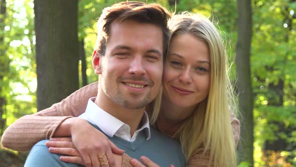 A Man Sits in a Park on a Sunny Day, a Woman Surprises Him with a Hug From Behind and They Smile