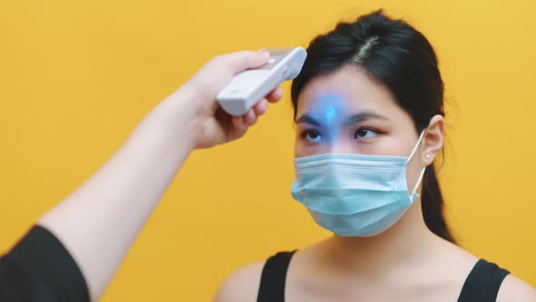 Young Asian Woman with Medical Mask Getting Her Body Temperature Checked with Laser Thermometer