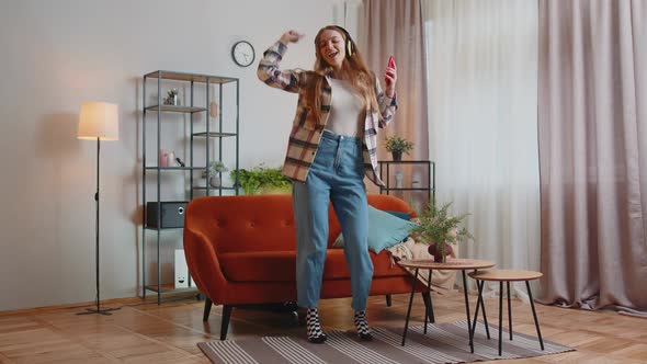 Pretty Caucasian Young Woman in Headphones Listening Music Dancing Singing in Living Room at Home