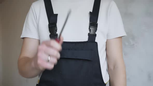 A Male Construction Worker in Overalls Shows a Flat Screwdriver To the Camera