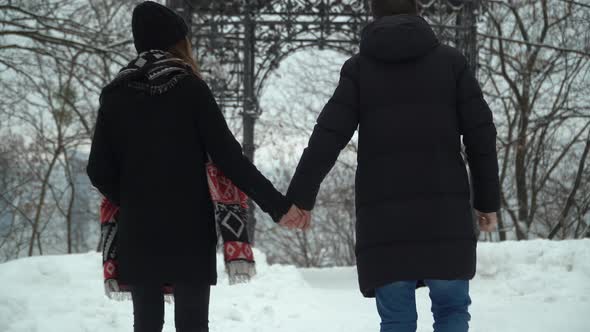 Young Man and Woman Walking in Winter Park Covered with Snow Holding Hands. Winter Leisure