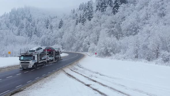 Aerial shot: cars and trucks are driving by the road in winter forest.