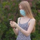 A young girl in a protective medical mask looks at the phone and sends messages - VideoHive Item for Sale