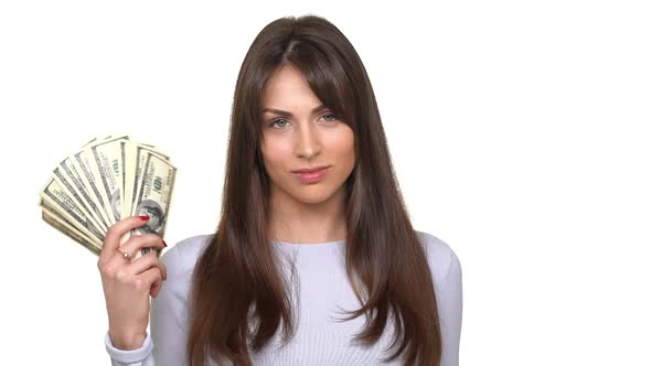 Concentrated Young Brunette Female Making Hand Fan From Sheaf of Dollars and Waving It Over White