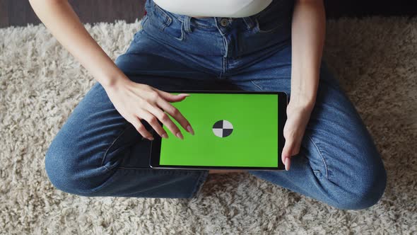 Woman in Jeans Sits in Lotus Position on Floor and Uses Electronic Tablet with Green Screen Top View