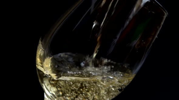 Wine is poured into a glass on a black background. Slow motion.