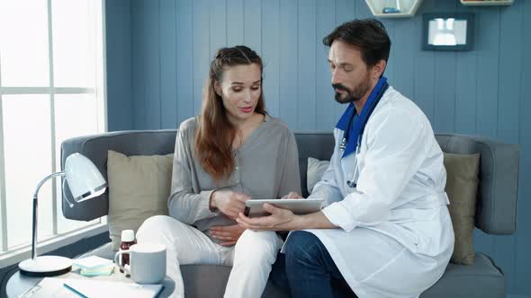 Male Gynecologist Explaining Tests Results To Pregnant Woman in Office.