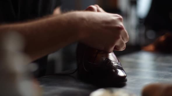 Tracking shot of male shoemaker tying laces on repaired and polished light brown leather shoes.