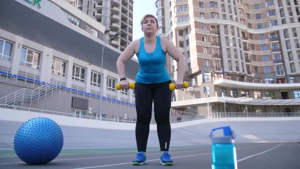 Overweight Female Training with Dumbbells Outdoors