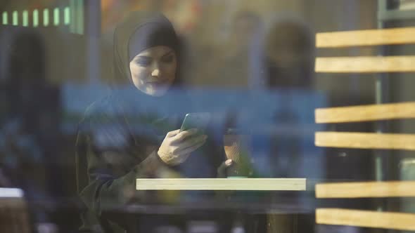 Beautiful Muslim Lady Drinking Coffee and Chatting on Phone, Sitting in Cafe