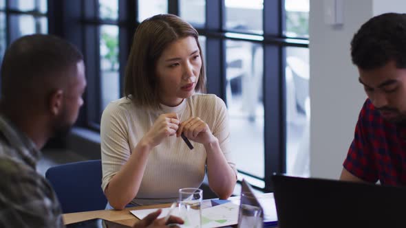 Diverse business people sitting using laptop going through paperwork in modern office