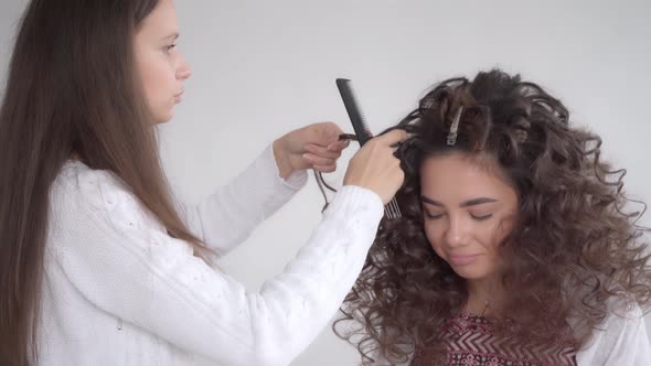 A hair stylist makes a hairstyle for a young beautiful girl with long dark hair